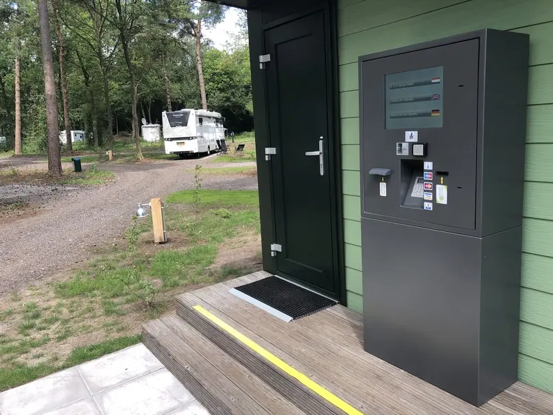 Ein grauer Check In Automat steht vor einer grünen Holzwand