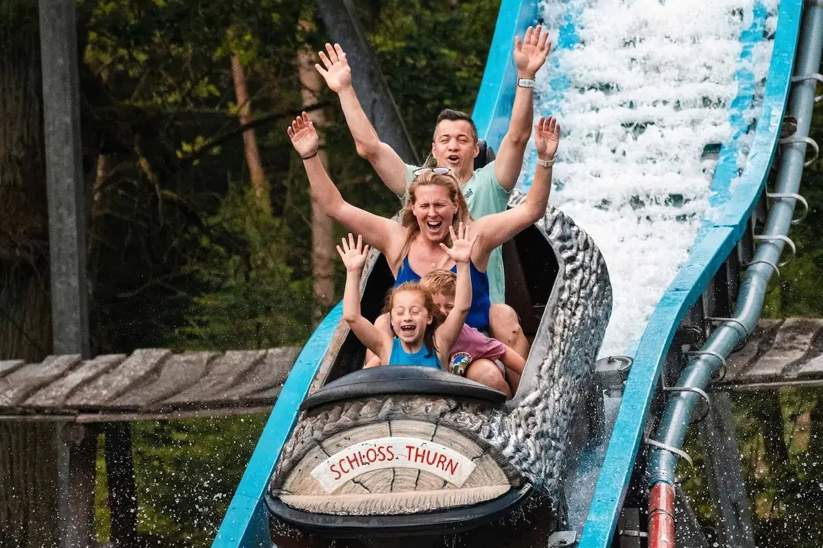 Zwei Kinder und zwei Erwachsene mit erhobenen Armen im Wagen der Wildwasserbahn