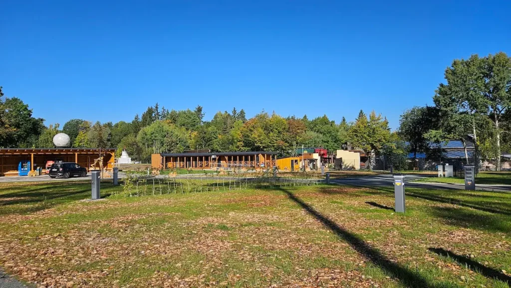 Blick auf Stellplätze im GlampingPark mit Sanitärgebäuden aus Holz und Wald im Hintergrund