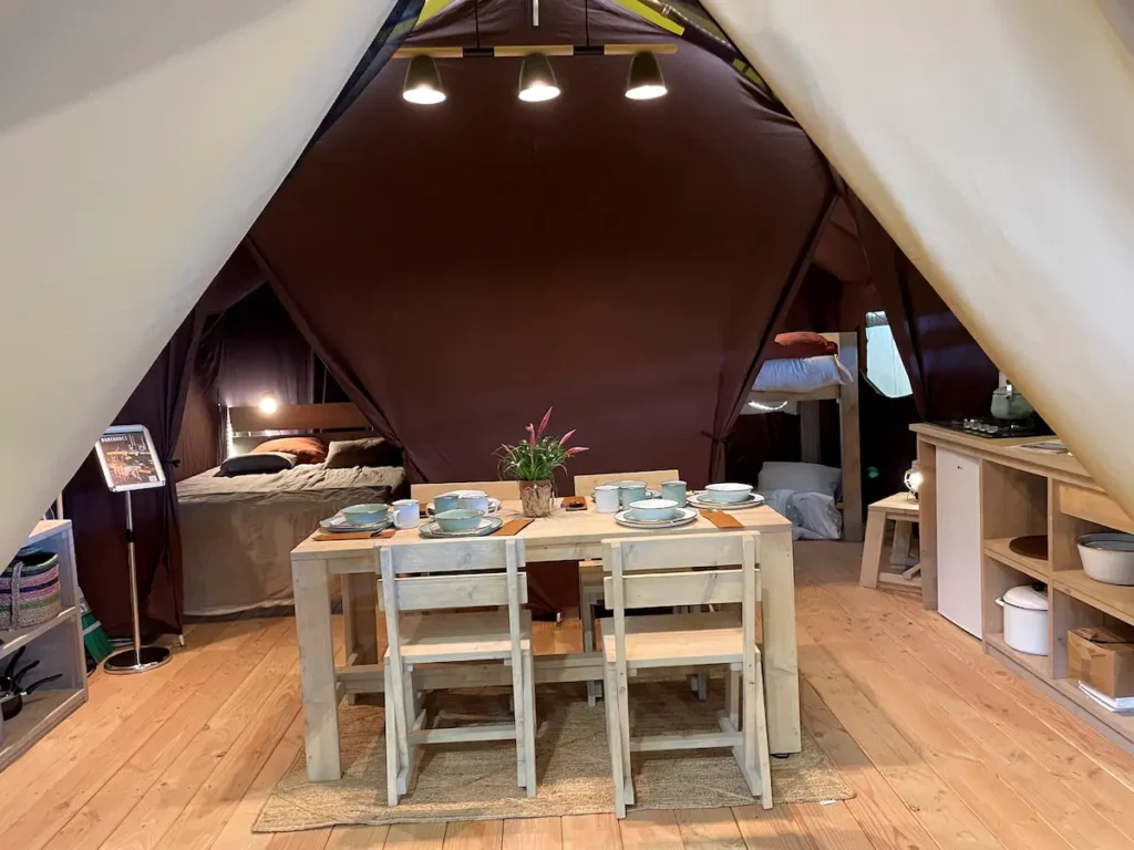 Innenbereich eines Safari Zeltes mit gedecktem Tisch und einem Blick in die Schlafbereiche