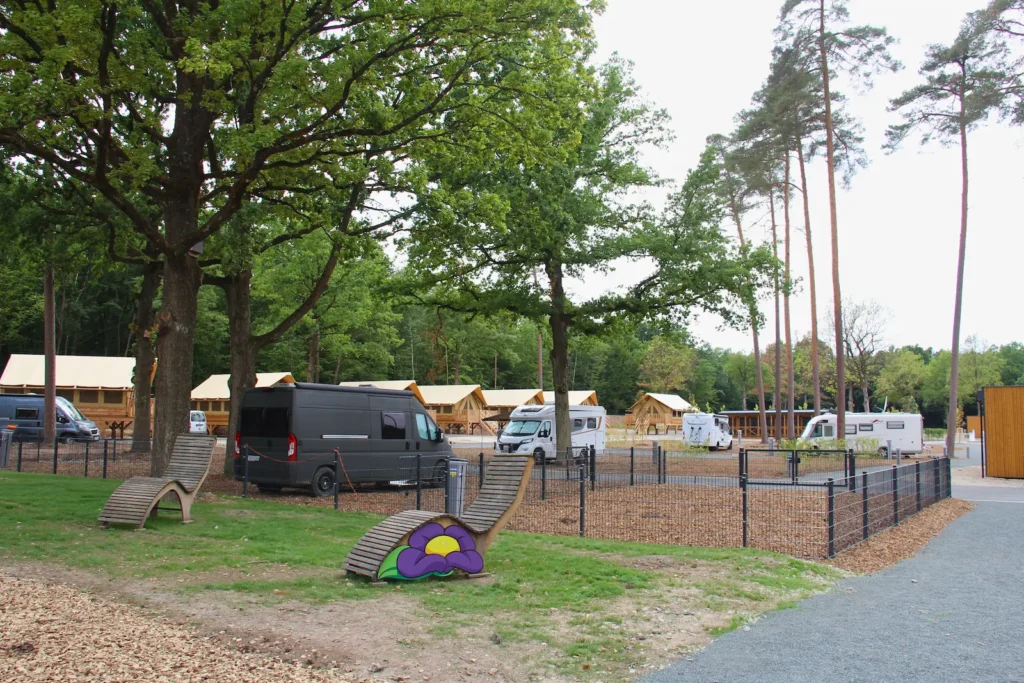 Zwei Holzliegen vor einem Campingstellplatz für Hunde mit Zaun