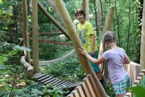 Zwei Kinder bewegen sich im Motorikpark auf Holzbrücken, Seilen und Holzstämmen