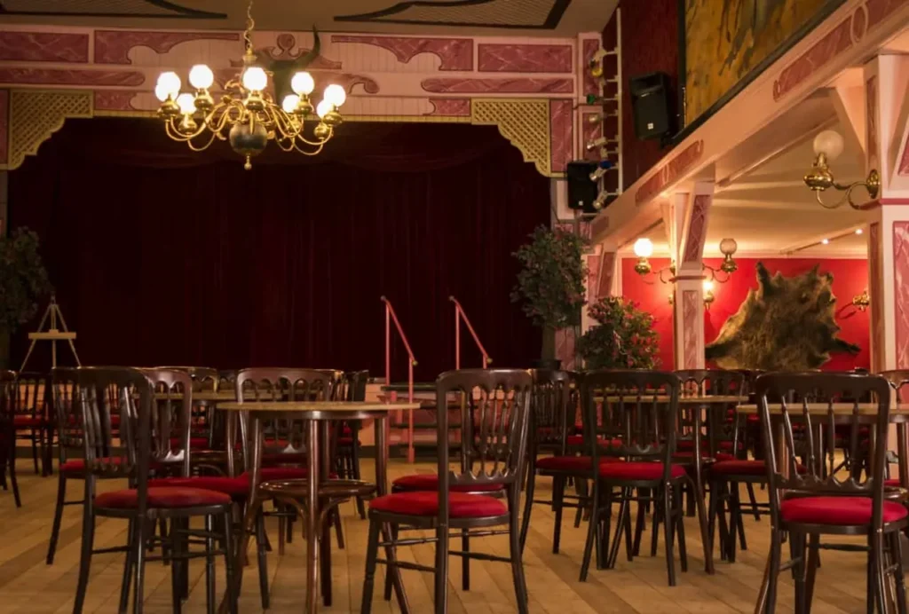 Innenansicht Saloon im Freizeitpark - ein großer Raum mit Essenstischen, Stühlen und einer großen Bühne