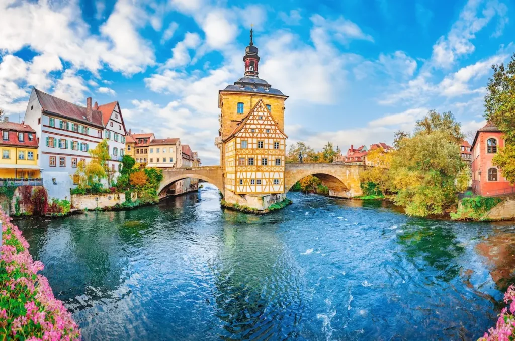 Ein Blick auf einen Fluss und eine Brücke in Bamberg mit blühenden Blumen und blauem Himmel