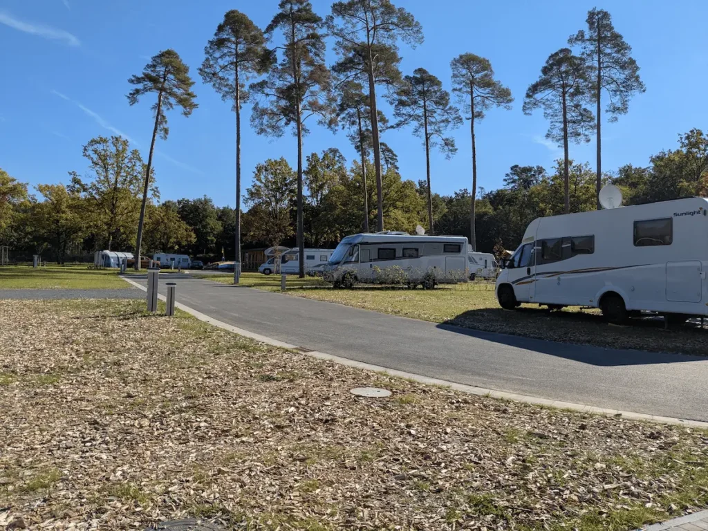 Mehrere Wohnmobile und Wohnwagen auf ihren Stellplätzen an einem Campingplatz mit Bäumen und blauem Himmel