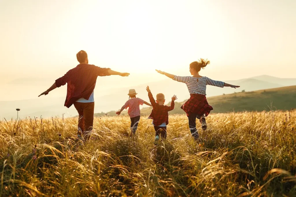 Eine Familie läuft mit zwei Kindern im Sonnenuntergang mit ausgestreckten Armen über ein Feld