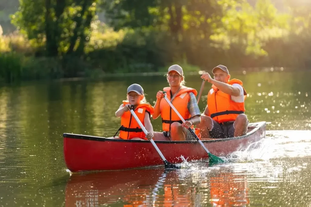Eine Familie mit Vater, Mutter und Kind sitzt mit Schwimmwesten in einem roten Kanu und fährt einen Fluss entlang