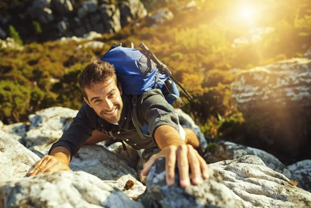 Ein Mann mit blauem Rucksack klettert eine steile Felswand nach oben