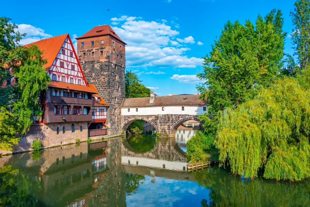 Blick auf die Altstadt von Nürnberg mit einem Turm, Fachwerkhaus und einer Brücke die sich im Wasser spiegelt